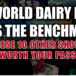 Holstein cow draped in Supreme Champion banner under Coliseum lights at World Dairy Expo, ringside crowd watching